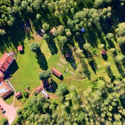 Odalgården sett från luften: röda byggnader och gröna gläntor omgivna av tät skog.