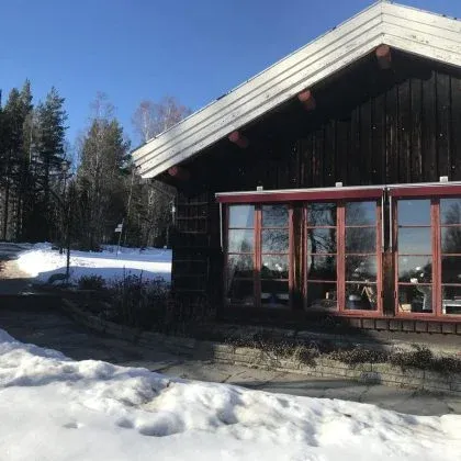Mörkpanelad byggnad med stora fönster, omgiven av snö.