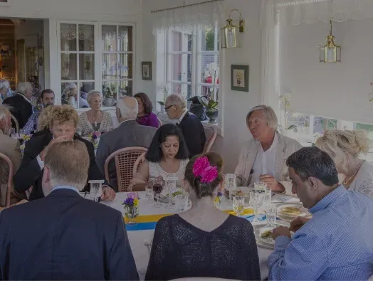 Sällskap som sitter och äter tillsammans vid ett dukat långbord.