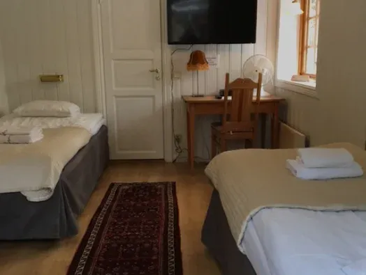 Tvåbäddsrum med bäddade sängar, skrivbord och tv på väggen.