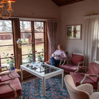 Sällskapsrum med fönster mot trädgården, fåtöljer och ett glasbord.