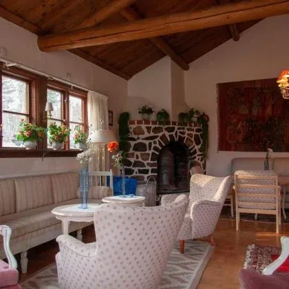 Salong med öppen spis av natursten, ljusa fåtöljer och blommor i fönstret.