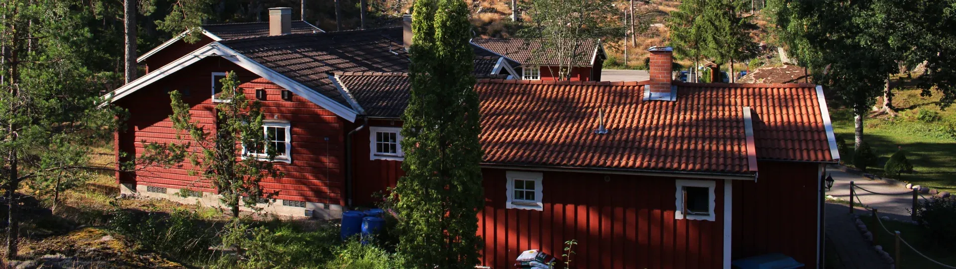 Röda stugor med vita fönsterfoder bland träden på området.